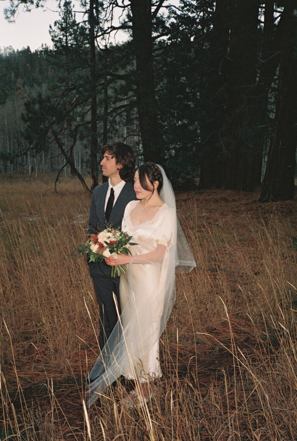 Bride and groom standing together in a forest, photographed on 35mm film